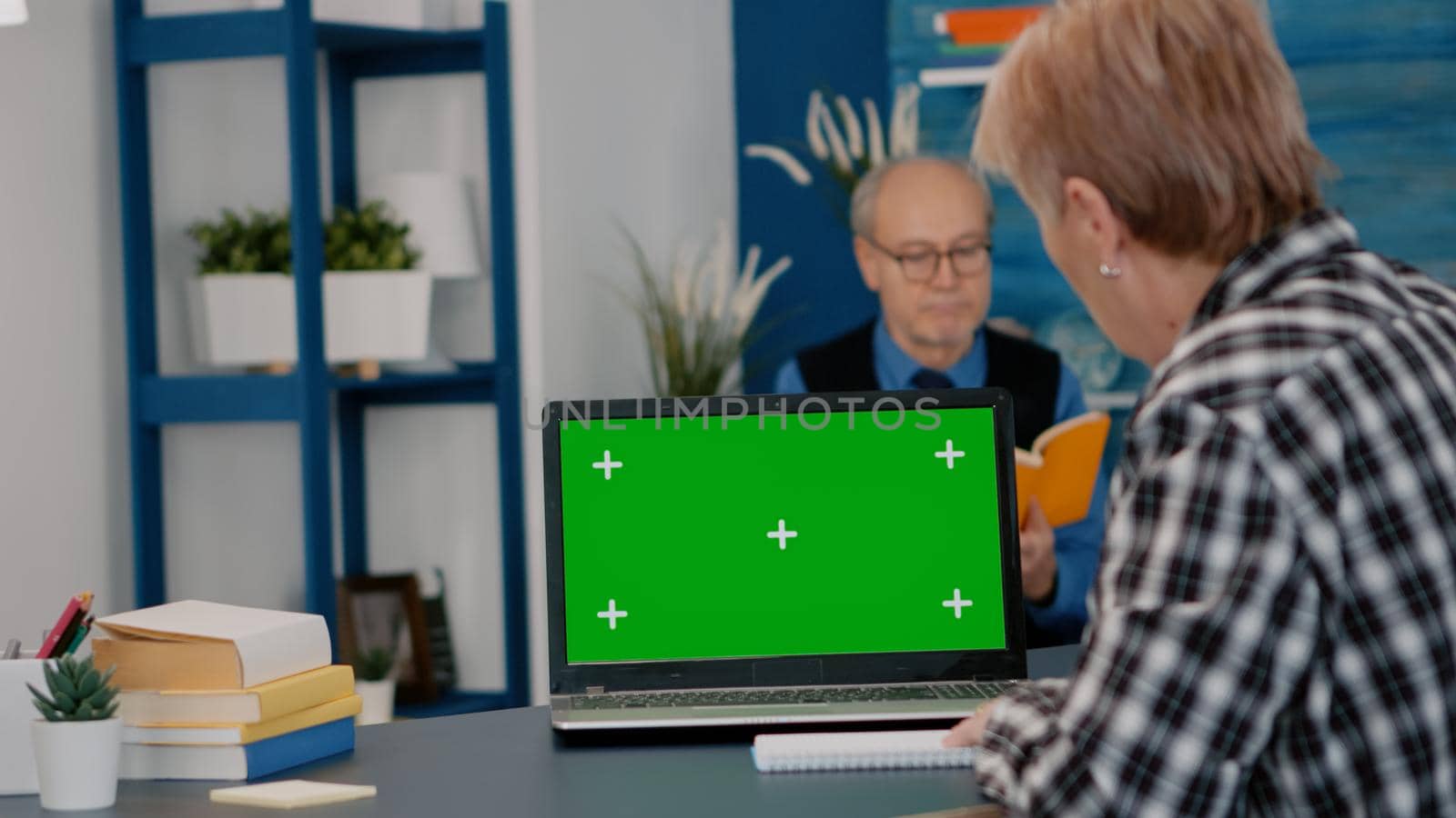 Elderly person reading on green screen, mock up, chroma key display of laptop, writing on notebook working from home. Senior woman watching at pc with isolated desktop, while man sitting on sofa