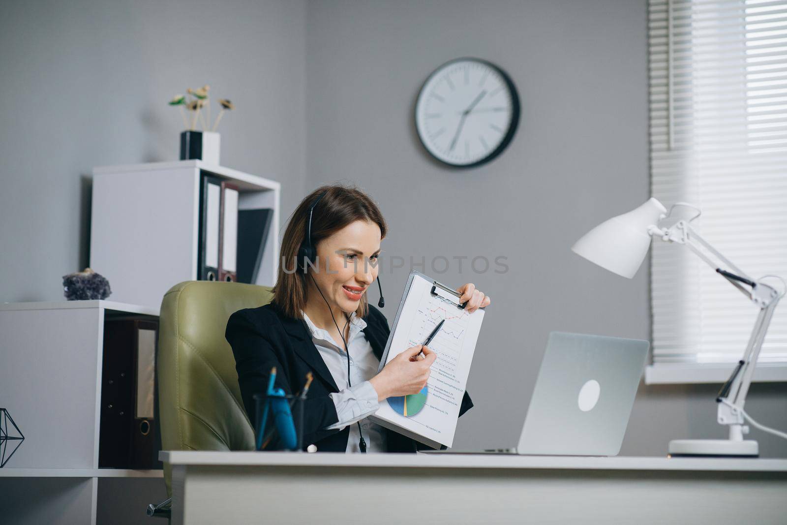 Businesswoman Holding Paper Financial Report Talk at Webcam make Video Call in Office, Business Coach Looking at Camera Speak Show Statistics Explain Marketing Strategy for Client, online training