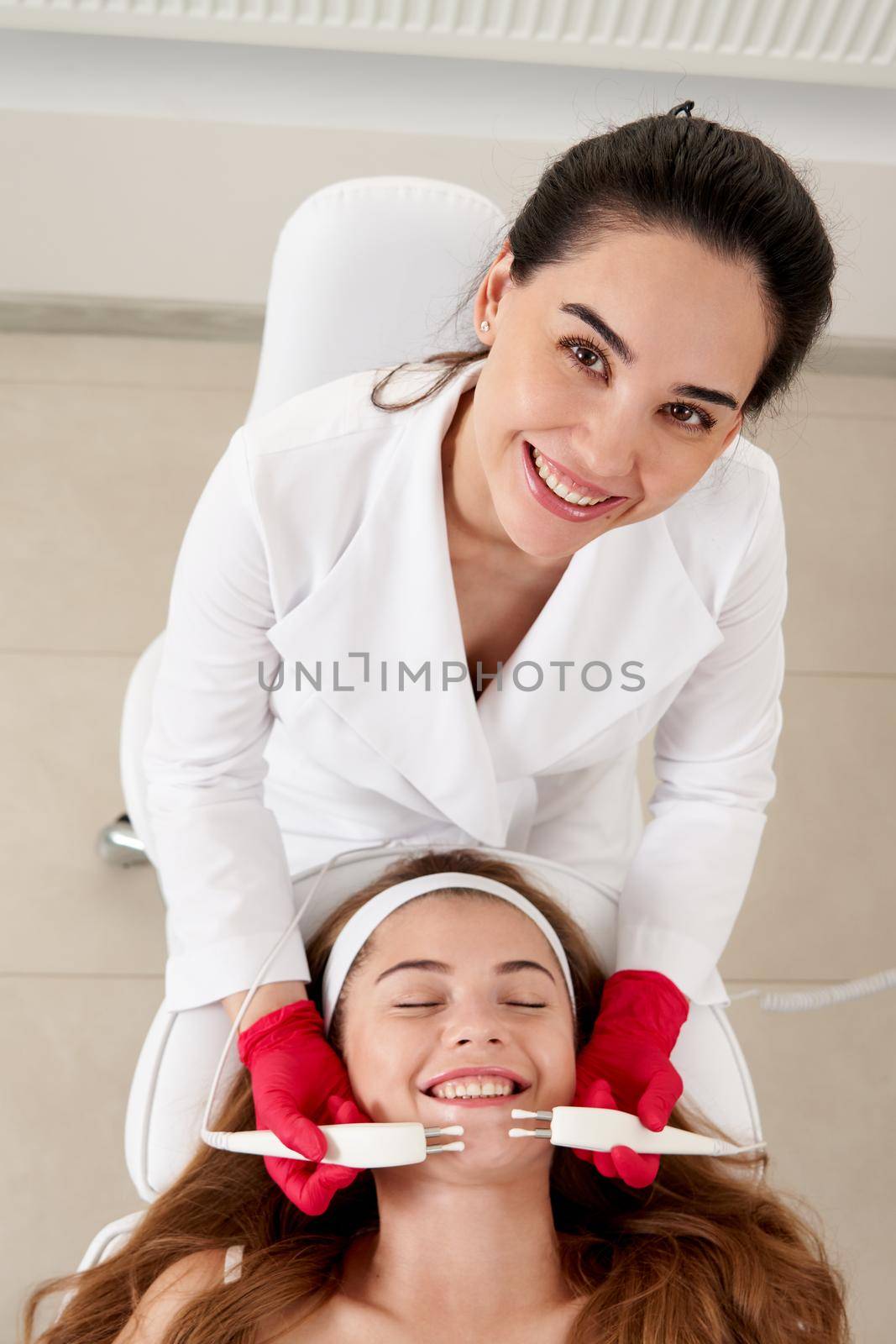 Beautiful Woman At Spa Clinic Receiving Stimulating Electric Facial Treatment From Therapist. Closeup Of Young Female Face During Microcurrent Therapy
