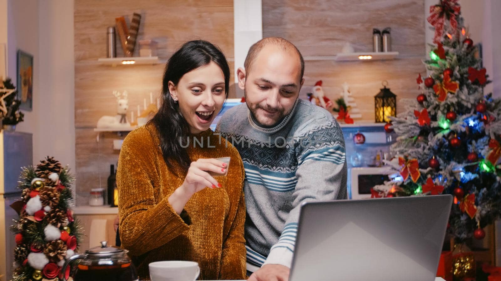 Cheerful couple doing online shopping for christmas gifts using credit card and laptop. Man and woman buying presents for winter holiday celebration. People preparing for festivity