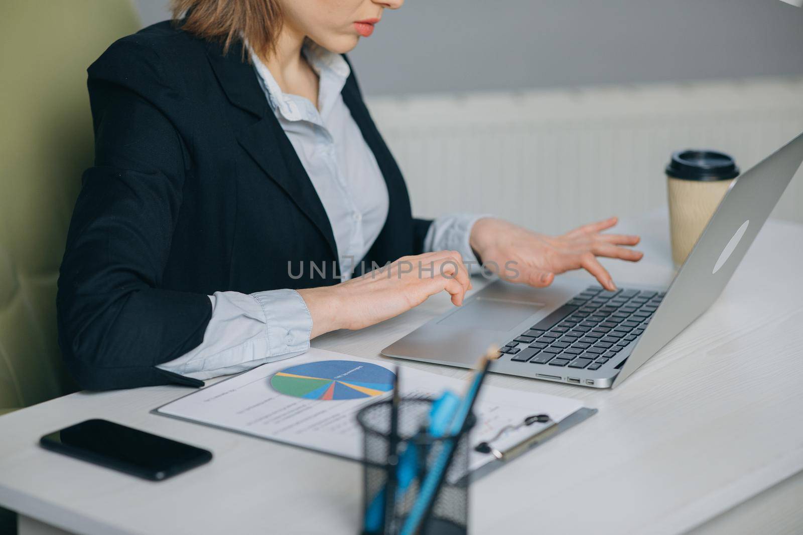 Close up of womans hands typing at laptop keyboard in office. Locked down close up shot. She is typing on her laptop keyboard