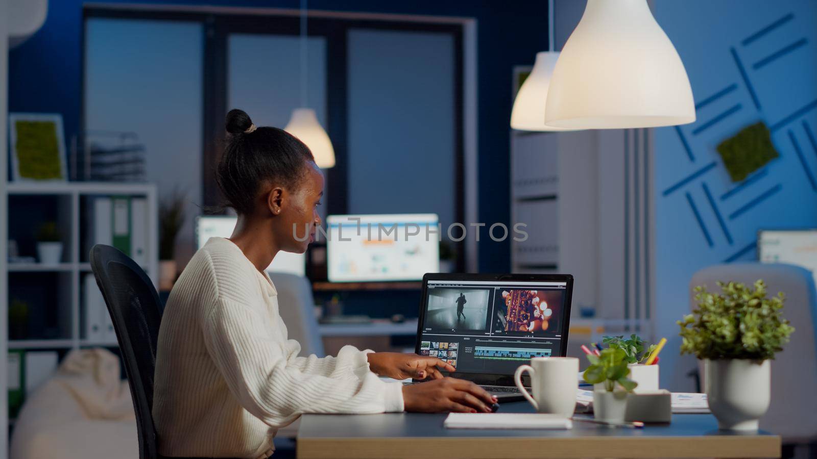 Black video editor working overtime at new project editing audio film montage sitting in start-up business office. Woman content creator using professional laptop, modern technology, network wireless