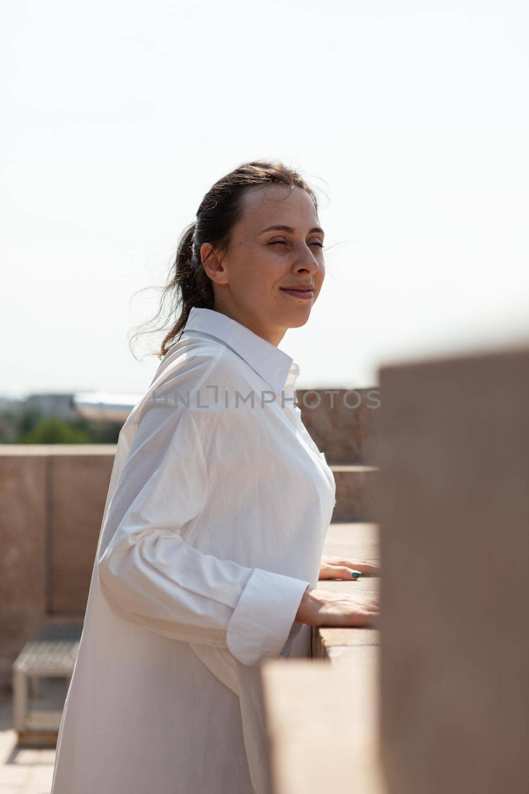 Happy caucasian female standing on tower rooftop enjoying seeing panoramic view of metropolitan city during summer vacantion. Landscape view of urban buildings from observation point. Travel concept