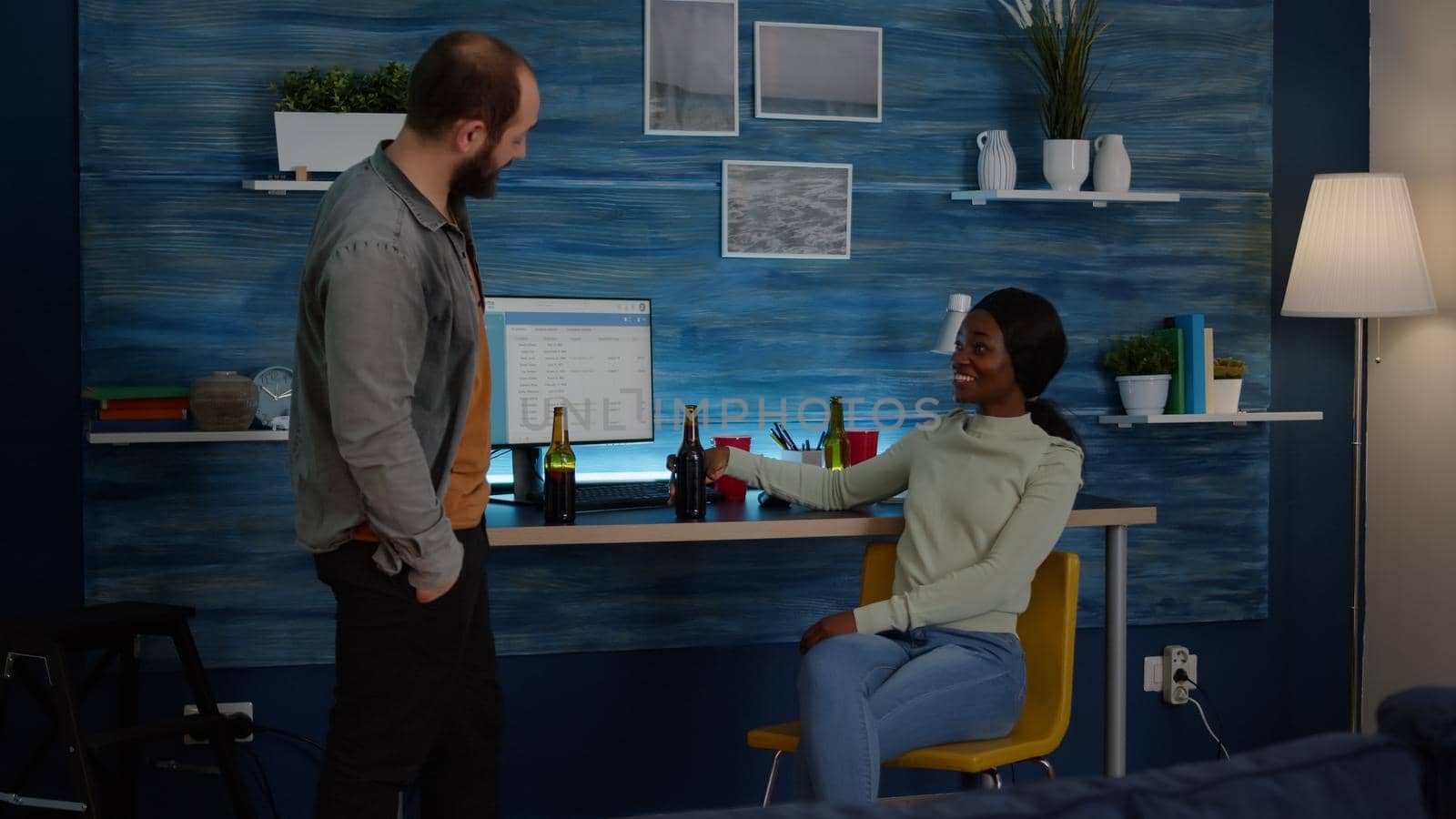 Happy man greeting his mixed race friends while talking with black woman in background. Mixed race people having fun, drinking beer enjoying time together in living room during night party