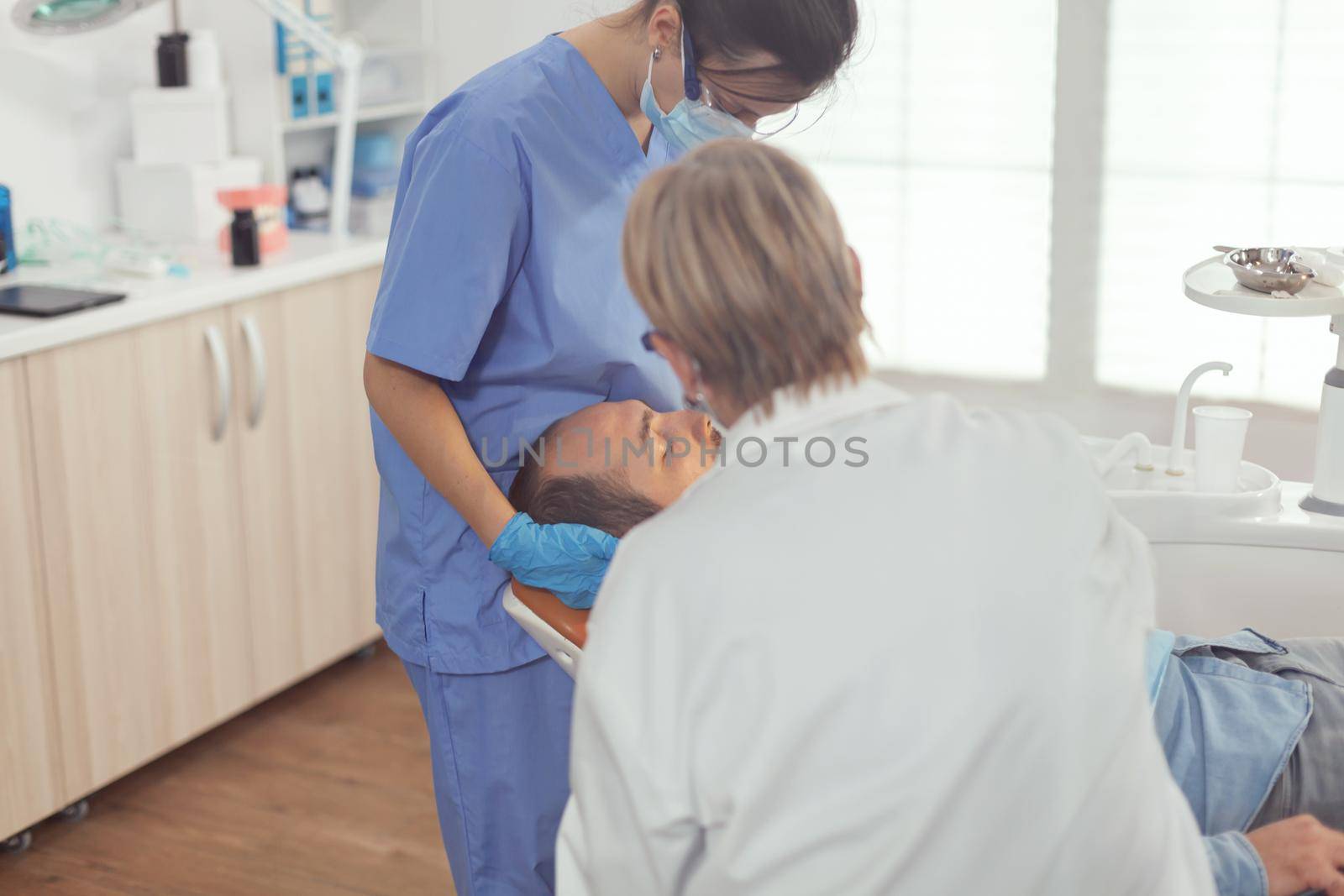 Sick man sitting on dental chair while senior doctor taking care of tooth health by DCStudio