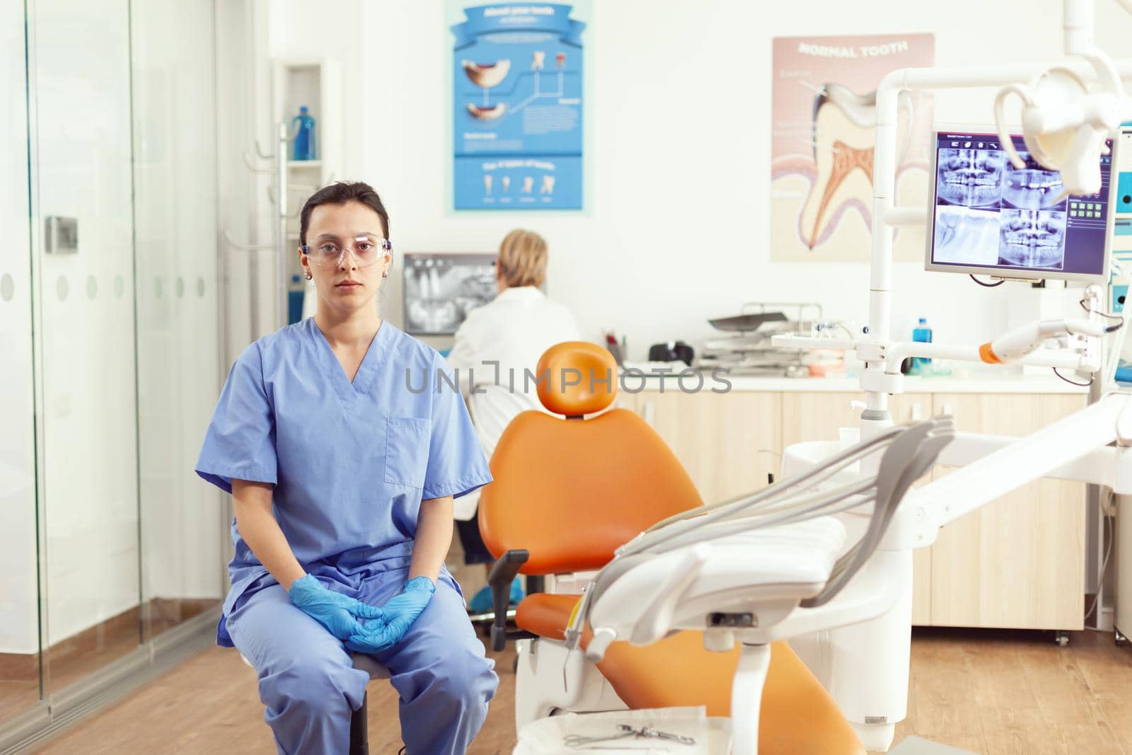 Closeup of medical assistant sitting on chair in hospital office waiting for sick man by DCStudio