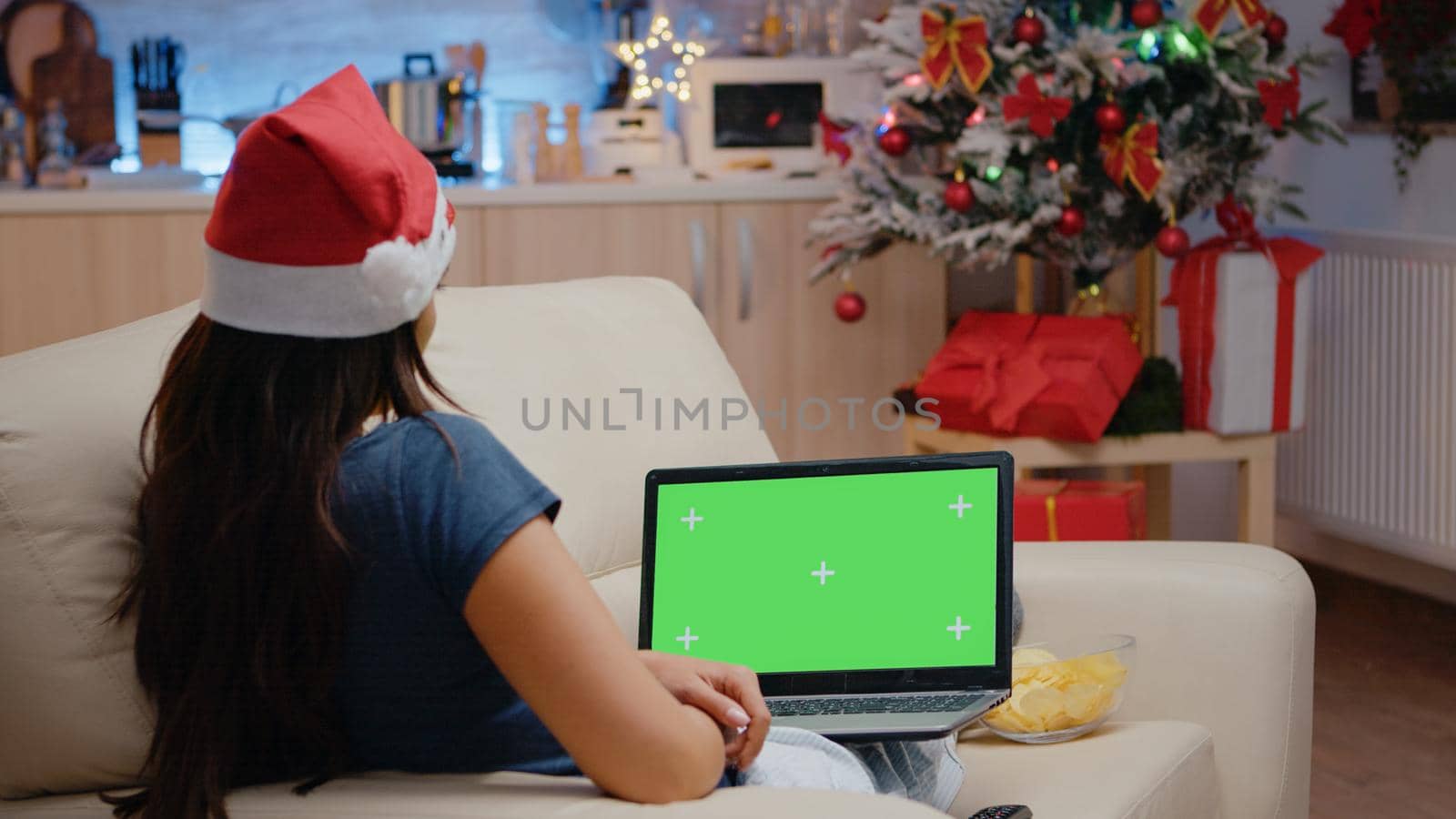 Woman looking at horizontal green screen on laptop on christmas eve. Festive adult watching chroma key on device, having mockup template and isolated background. Person with gadget