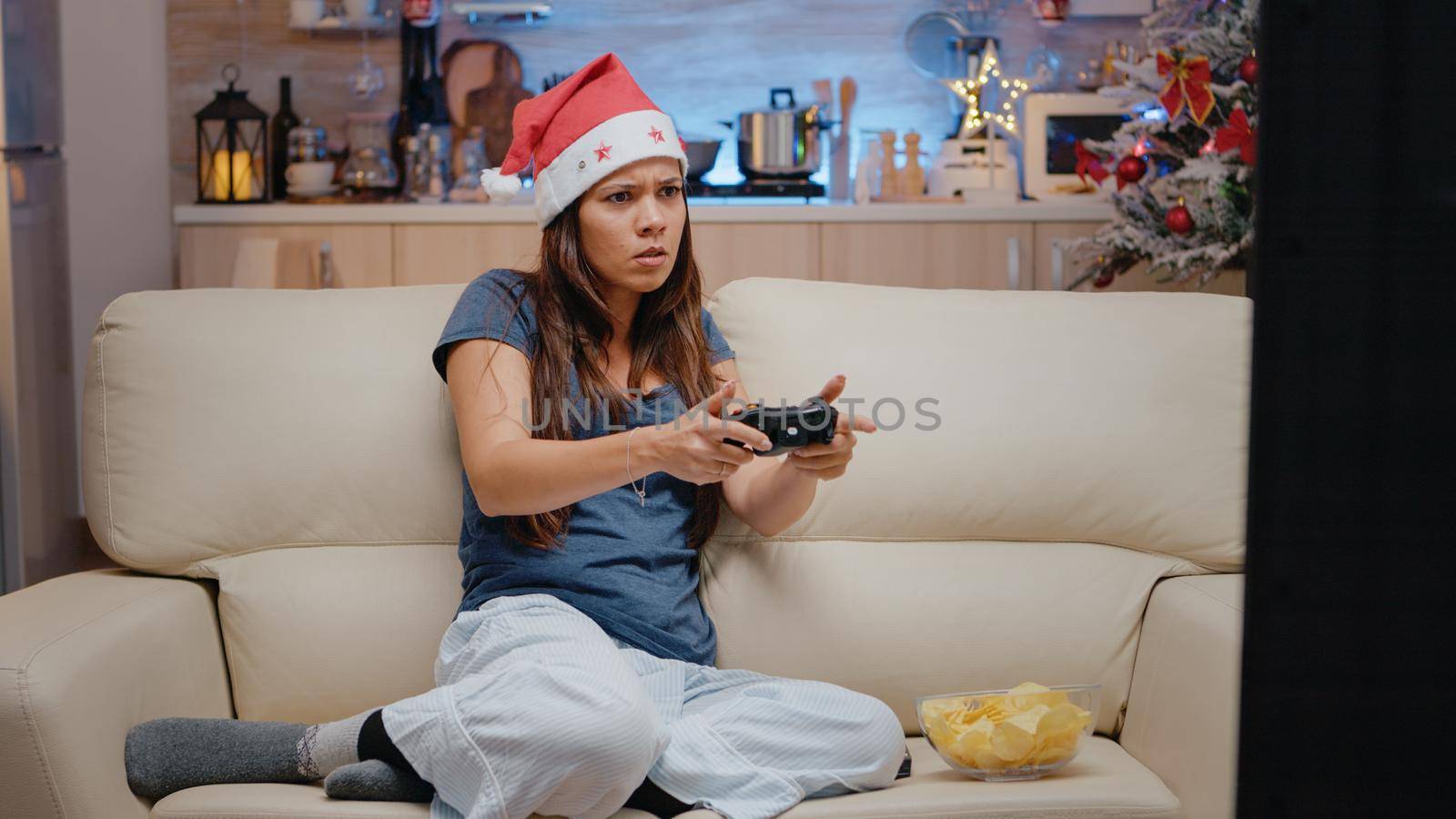 Unhappy adult losing at video games with joystick on tv console. Woman playing online game using controller at television on christmas eve for holiday celebration. Festive person