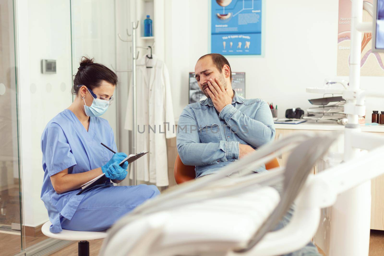 Dentistry nurse writing notes on clipboard about patient dental problems waiting for doctor orthodontist. Assistant sitting in stomatological room preparing for tooth examination before surgery