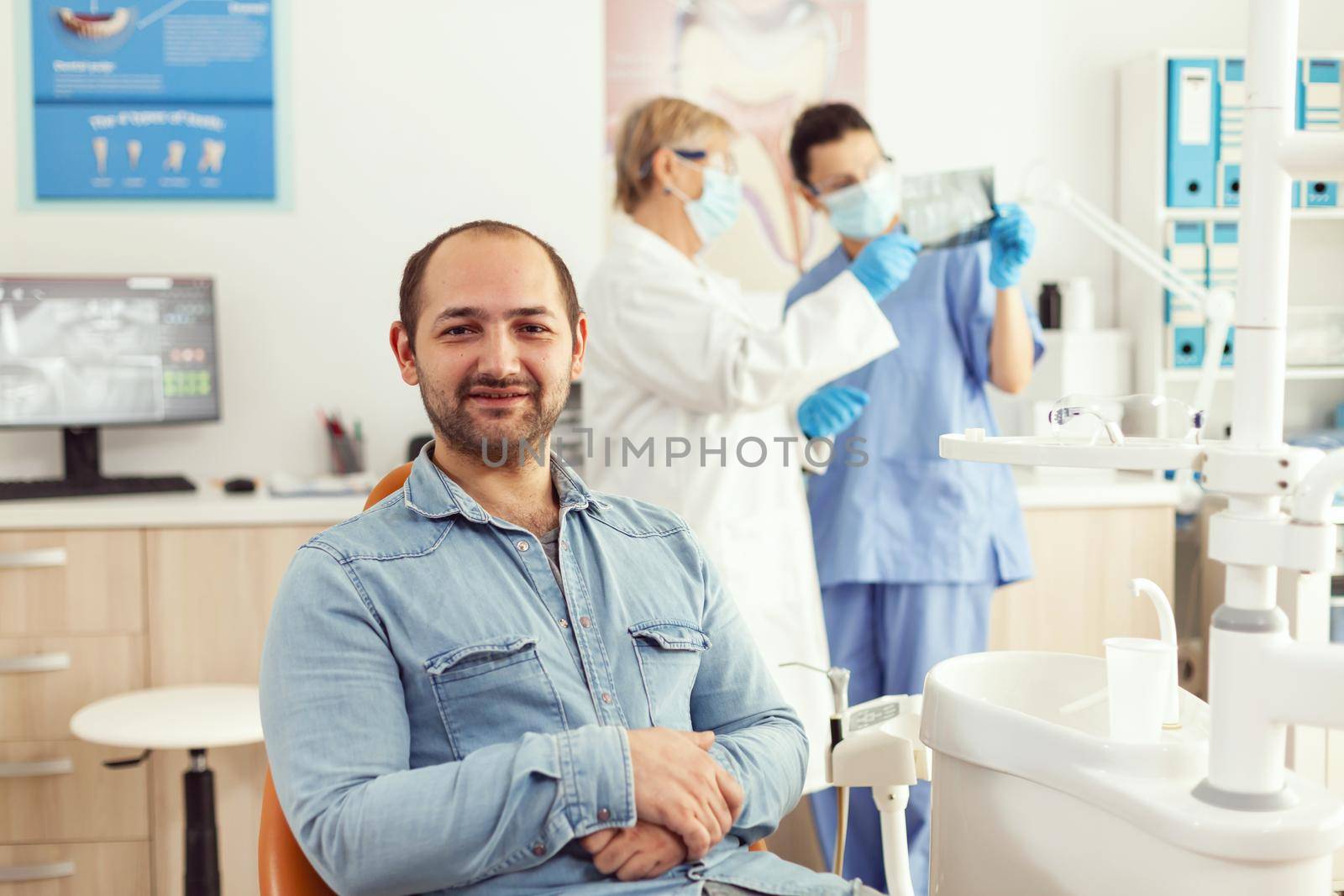 Portrait of man patient sitting on dental chair preparing for stomatology consultation waiting for somatology treatment. Senior woman doctor and medical nurse examining orthodontic x-ray