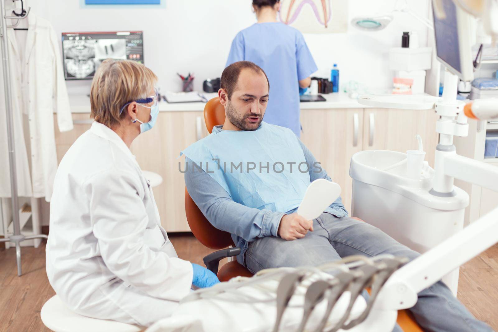 Man patient looking in mirror after medical stomatological team finising dental surgery during stomatology procedure. Senior doctor explaining healthcare treatment for toothache pain