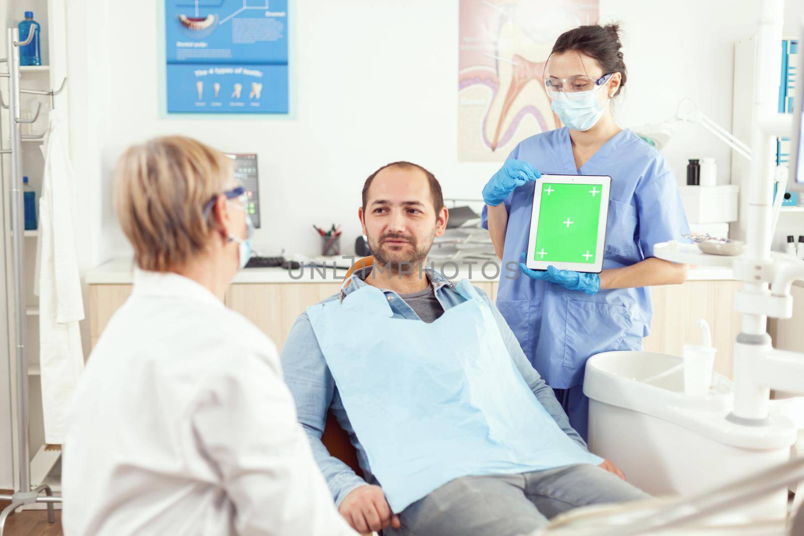 Stomatology nurse pointing her hand on mock up green screen chroma key tablet by DCStudio