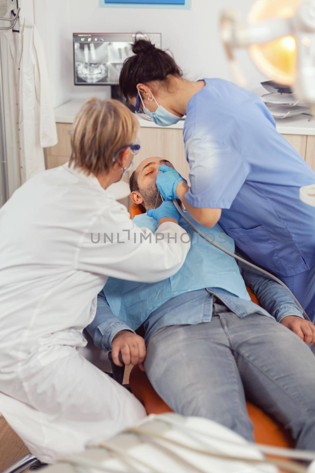 Senior woman dentist checking with mirror sick patient health. Medical nurse preparing for cleaning teeth, treating affected mass while sick man sitting on stomatology chair during examination