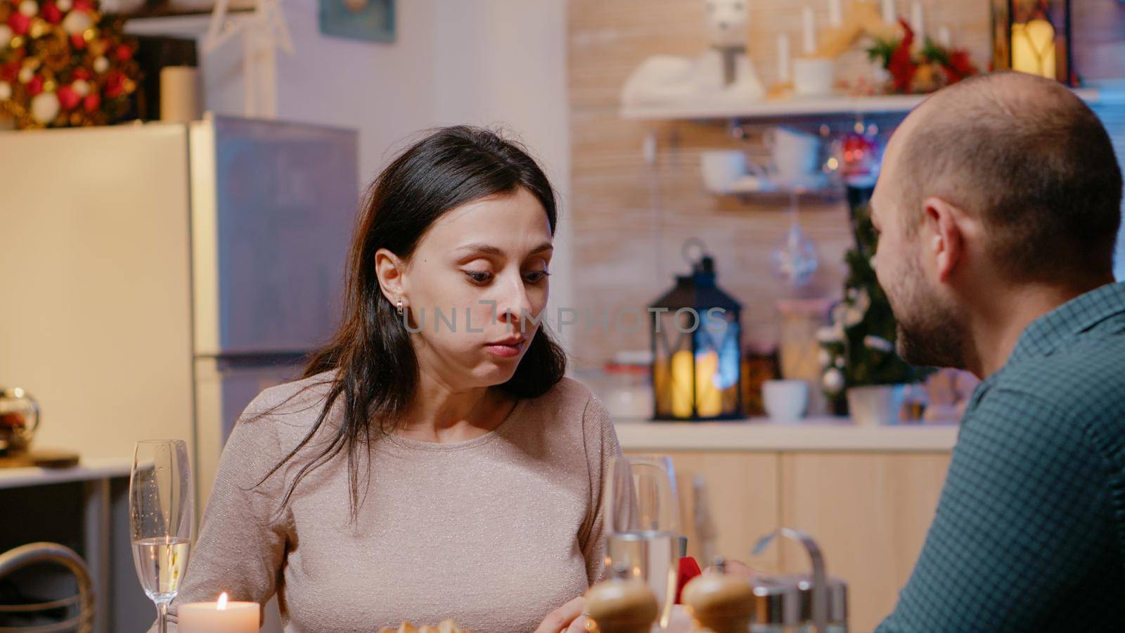 Close up of cheerful woman getting asked to marry partner at christmas eve dinner. Man proposing to young adult with engagement ring while enjoying festive meal. Engaged couple on holiday