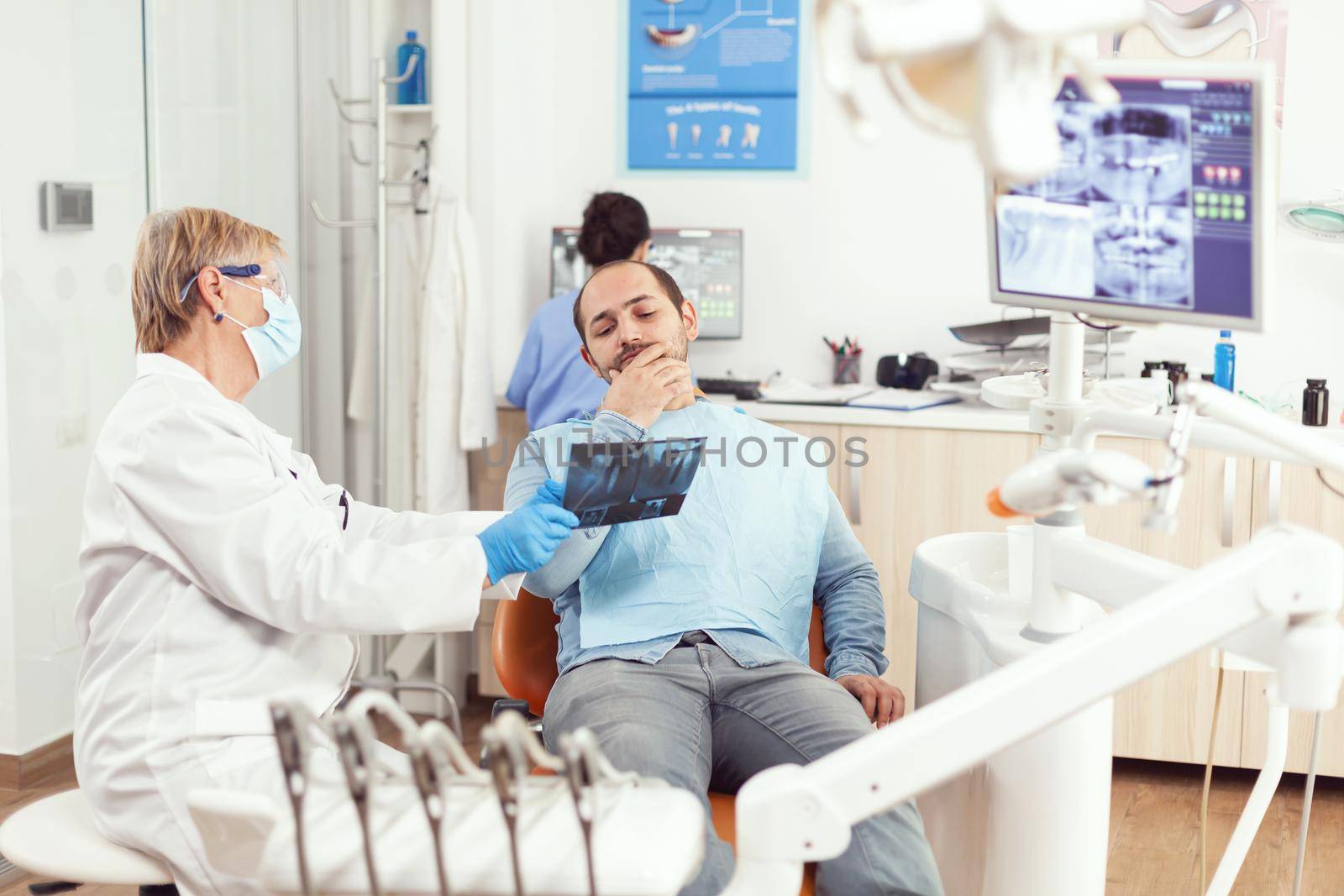 Senior woman dentist examining tooth radiography with sick man by DCStudio