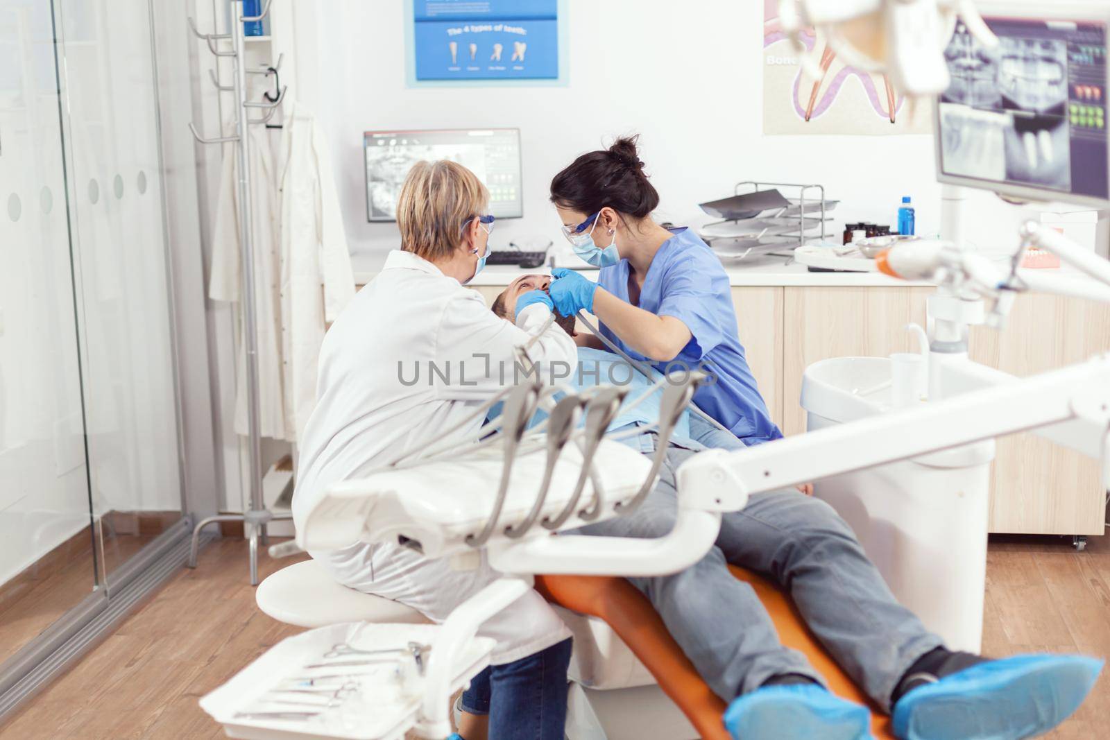 Hospital dentists team cleaning teeth of sick man preparing for stomatology surgery during stomatological inspection. Patient sitting on dental chair waiting for orthodontic inspection