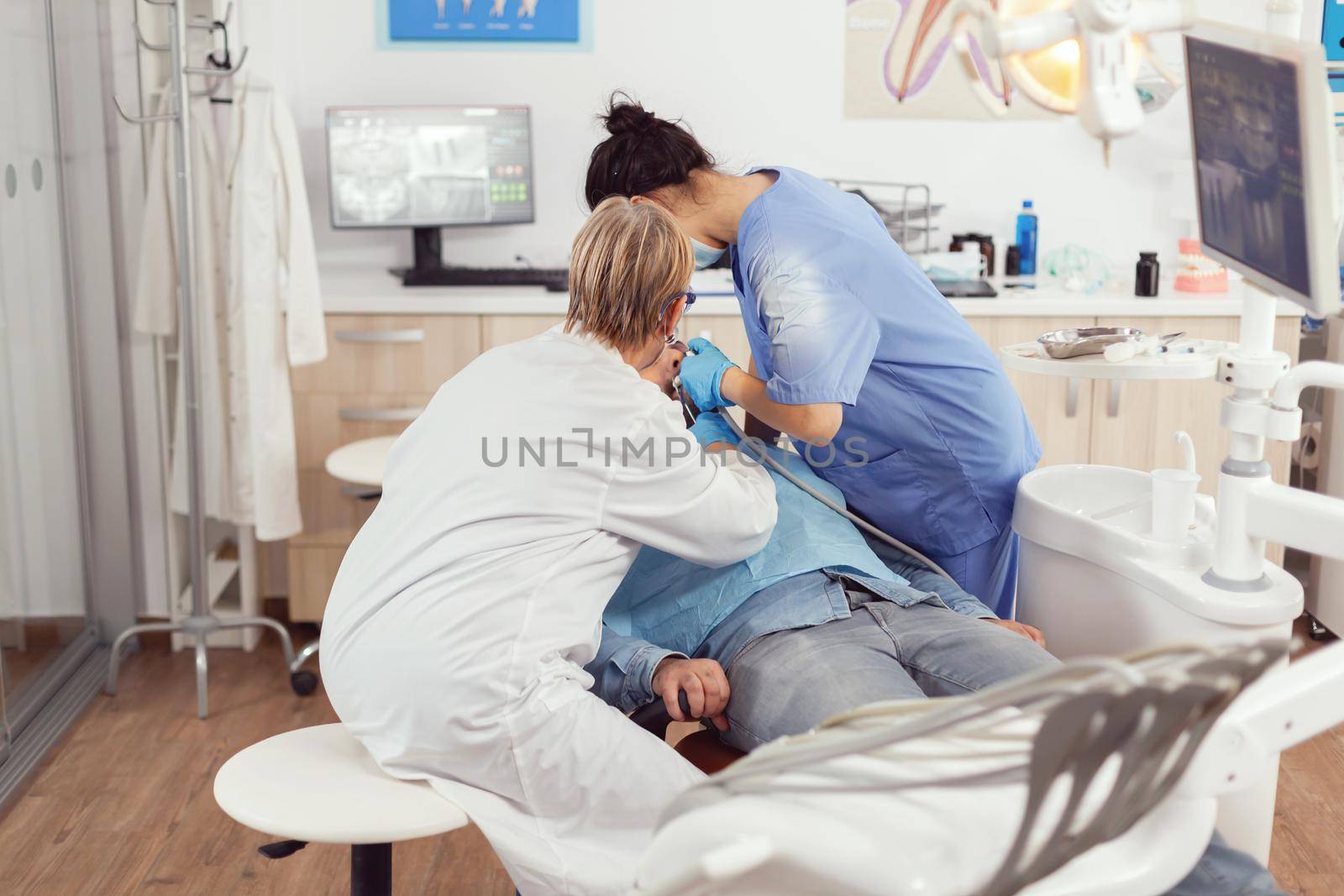 Senior woman dentist technician looking at mouth patient examining sick man by DCStudio