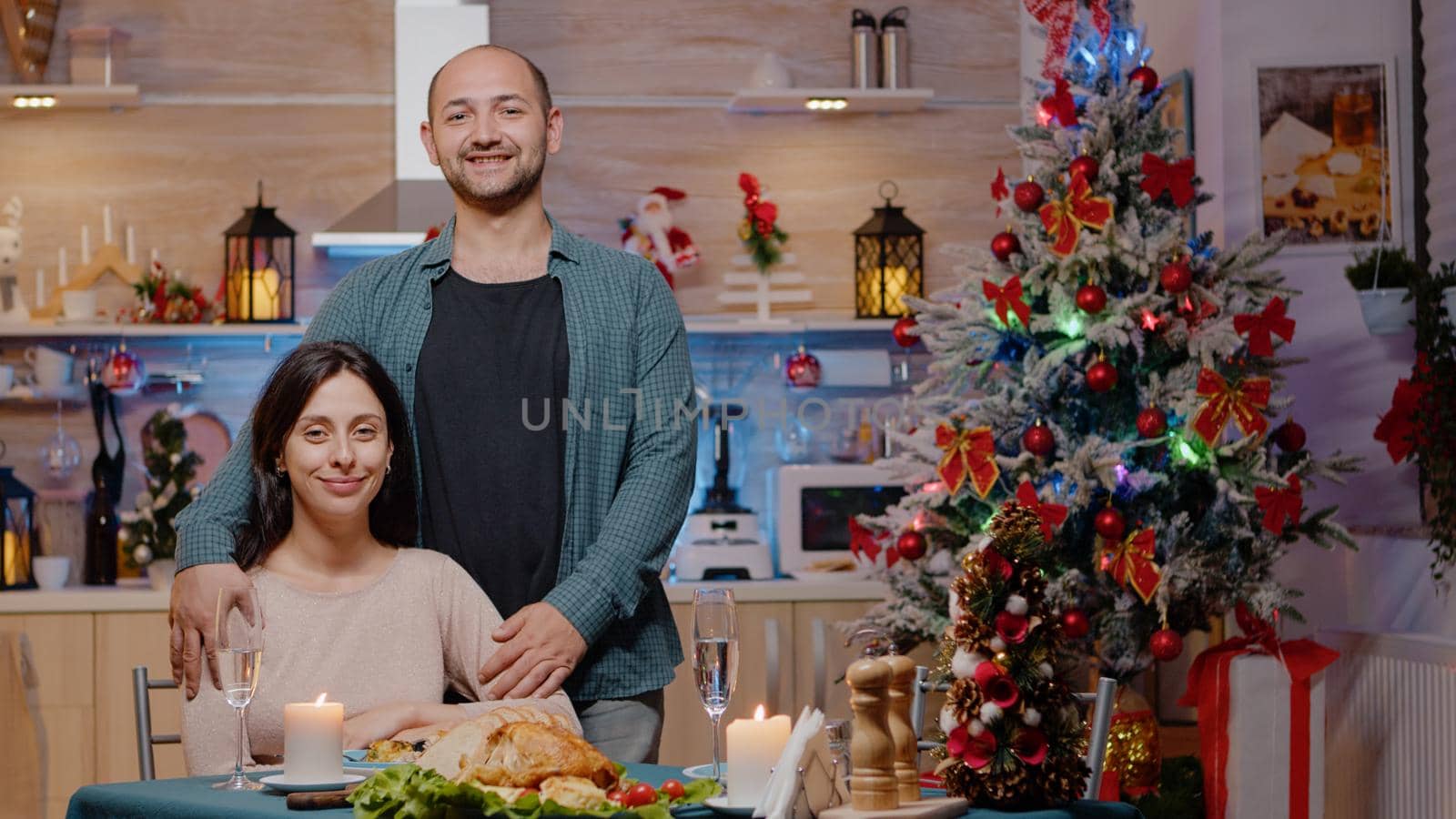 Portrait of couple at festive dinner on christmas eve. Man and woman looking at camera while enjoying holiday meal and celebration, sitting together and feeling cheerful for winter festivity