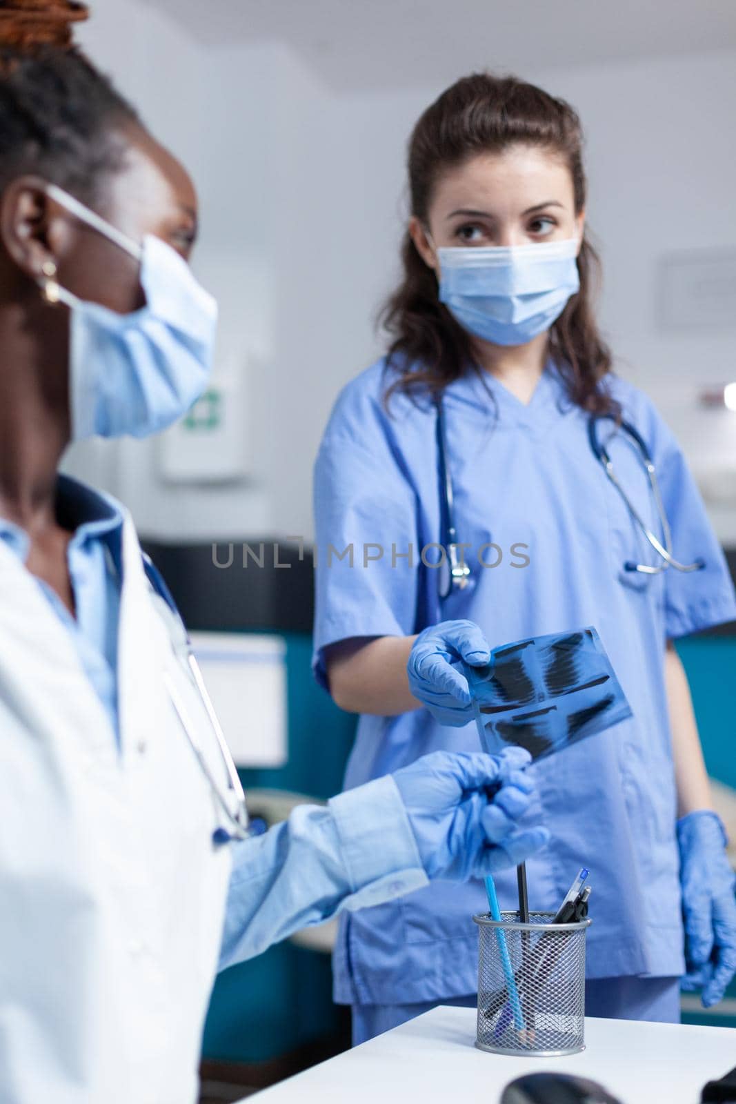 Practitioner nurse giving xray to african american radiologist doctor examining lungs disease during clinical appointment in hospital office. Medical team with protective face masl against covid19