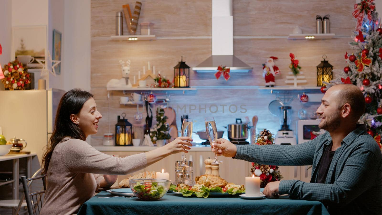 Couple raising glasses of champagne celebrating christmas eve. Festive man and woman sitting at table eating chicken and drinking alcohol for traditional dinner on seasonal holiday.