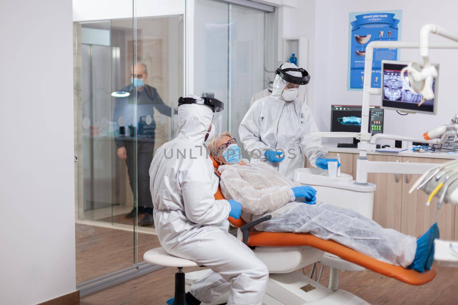 Senior patient wearing hazmat suit during coronavirus in dentist office Elderly woman in protective uniform during medical examination in dental clinic.
