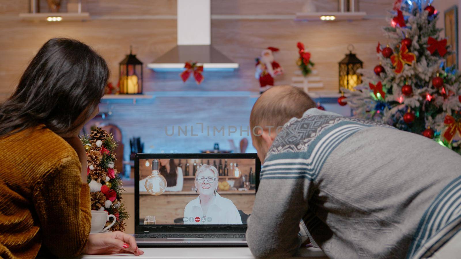 Festive couple talking to elder woman on video call using laptop for remote communication on christmas eve. People chatting with senior mother on online conference for holiday festivity