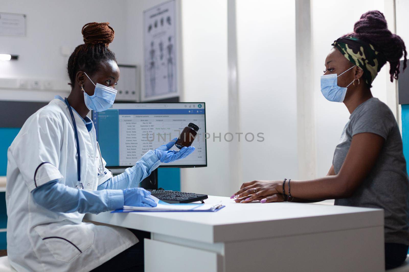 African american therapist doctor holding pills bottle explaining medication treatment to sick patient during clinical appointment in hospital office. Physician medic discussing sickness symptoms