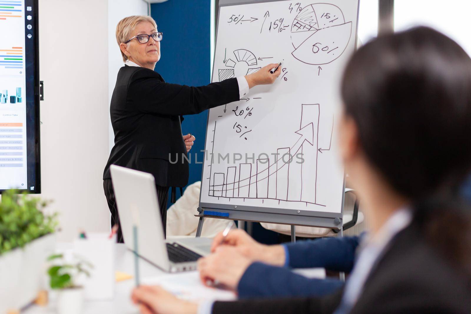 Mature businesswoman writing on white board, presenting sales evolution by DCStudio