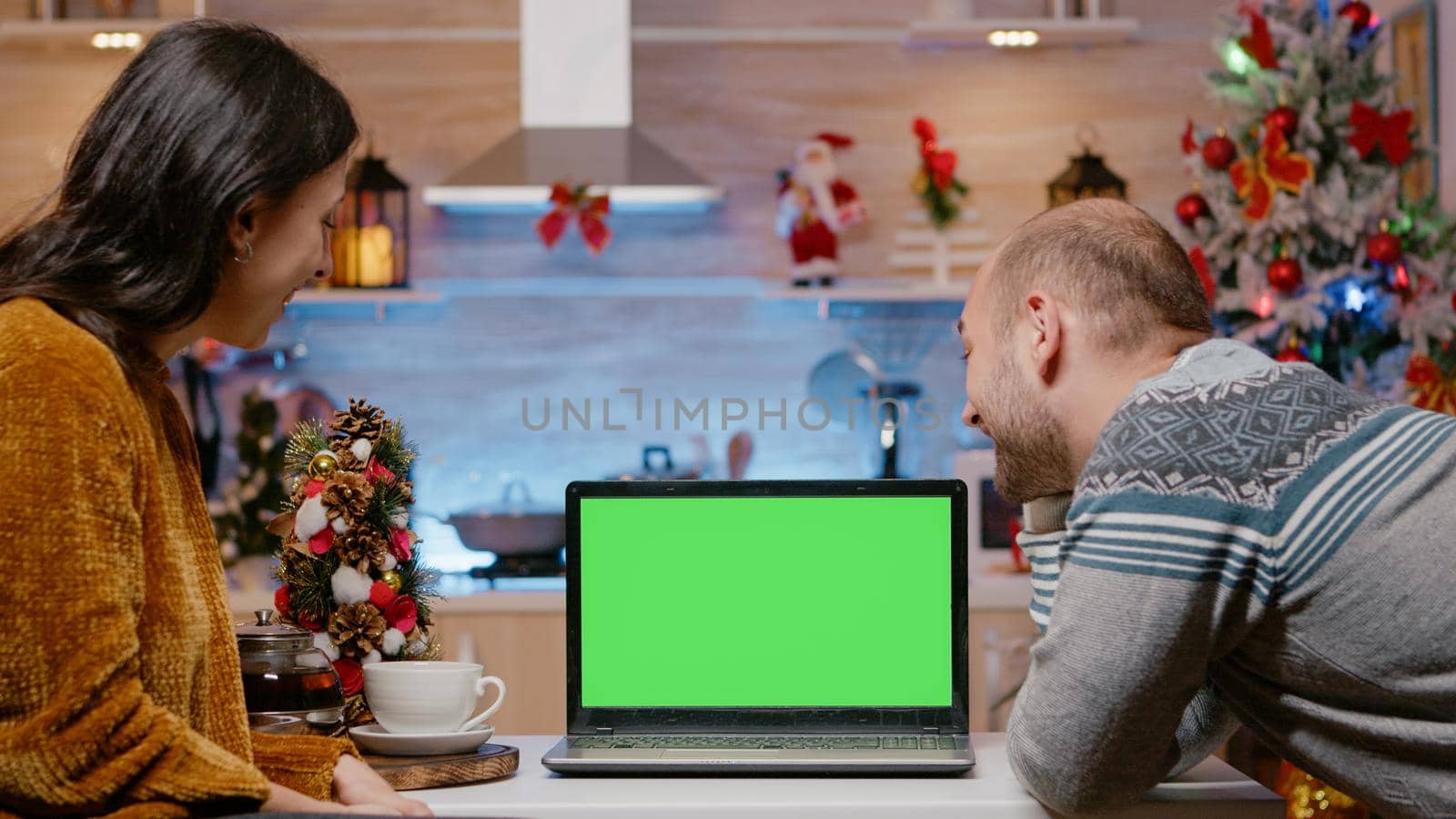 Festive couple looking at horizontal green screen on laptop for christmas eve celebration. People with chroma key and isolated mockup template preparing for seasonal holiday festivity.