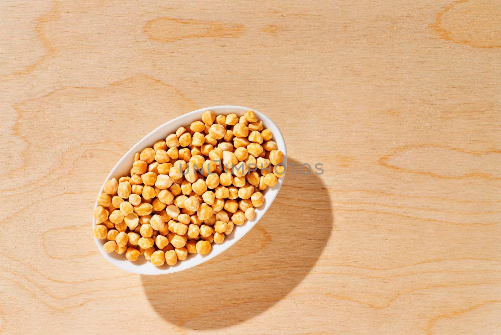 Top view of dried chickpeas in white bowl on wooden background