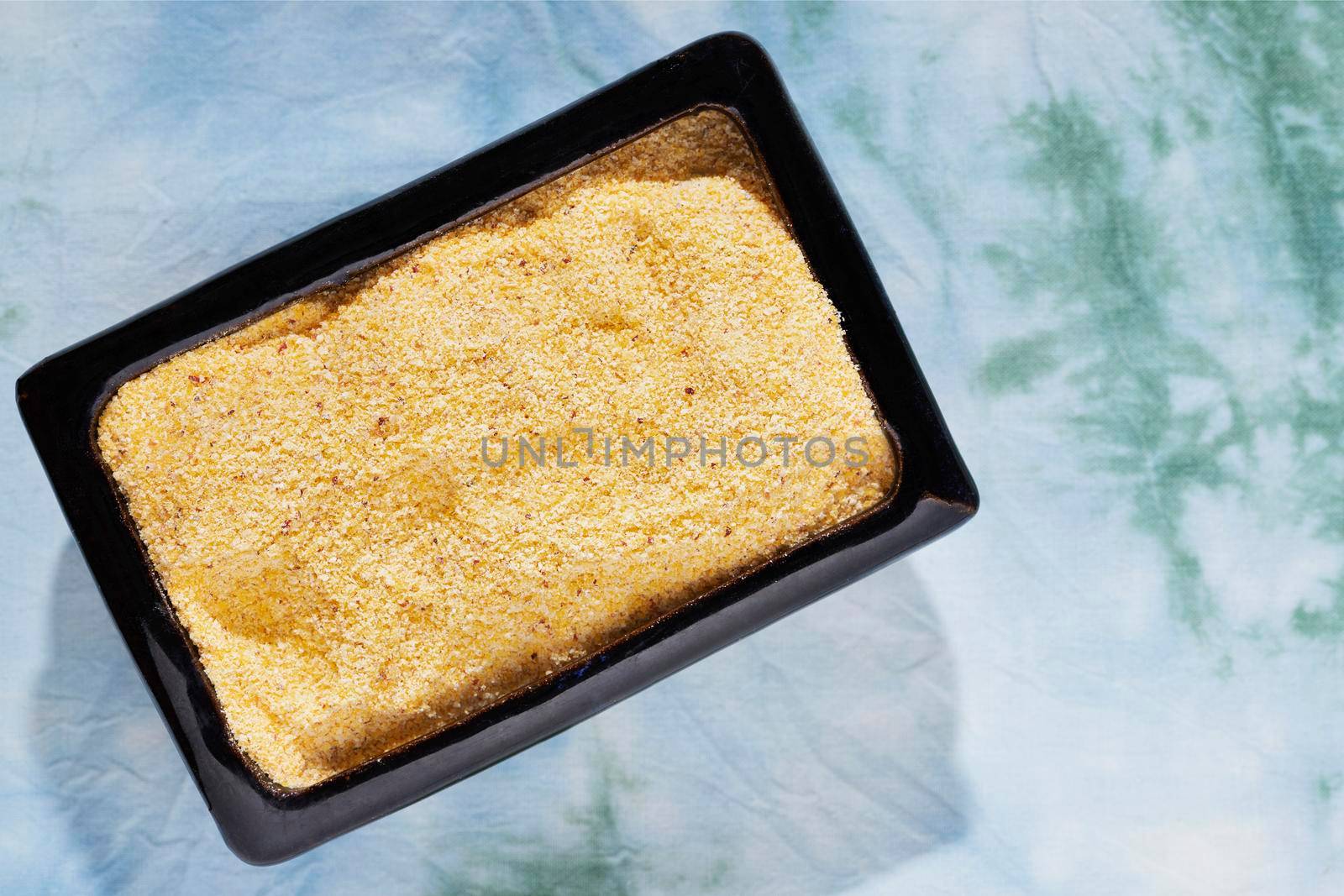 Heap of  uncooked polenta in blue bowl, yellow grains of cornmeal 