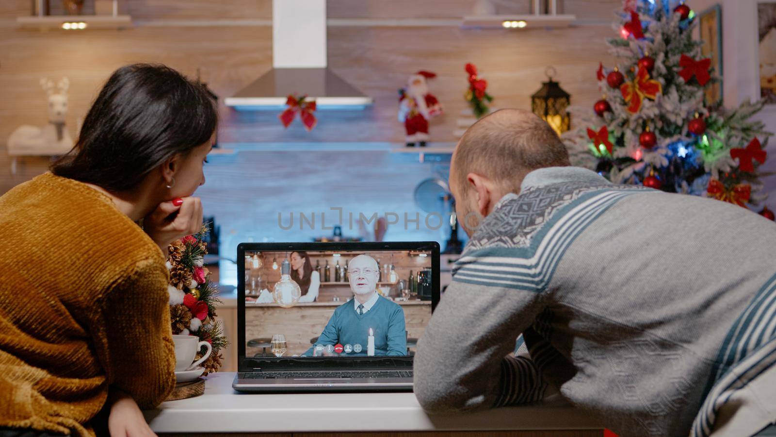 Couple using video call conference with father on christmas eve. Man and woman feeling festive while talking to elder person for remote communication on laptop. Seasonal holiday festivity