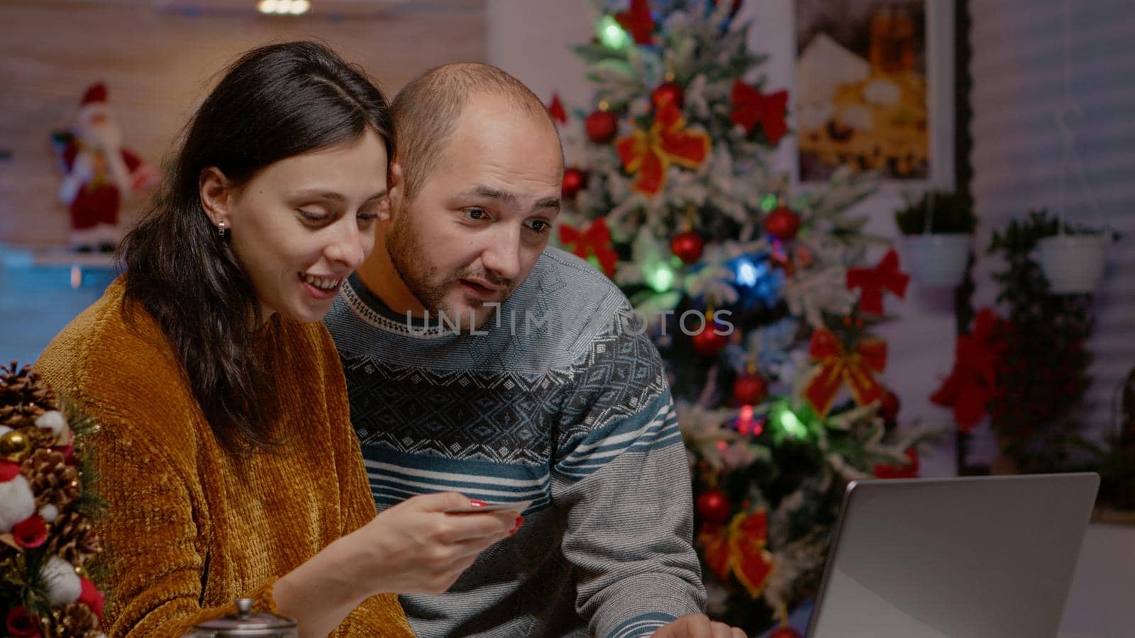 Couple using laptop and credit card for christmas shopping online to give presents to family at dinner celebration. Cheerful people buying gifts for seasonal holiday festivity. Festive season