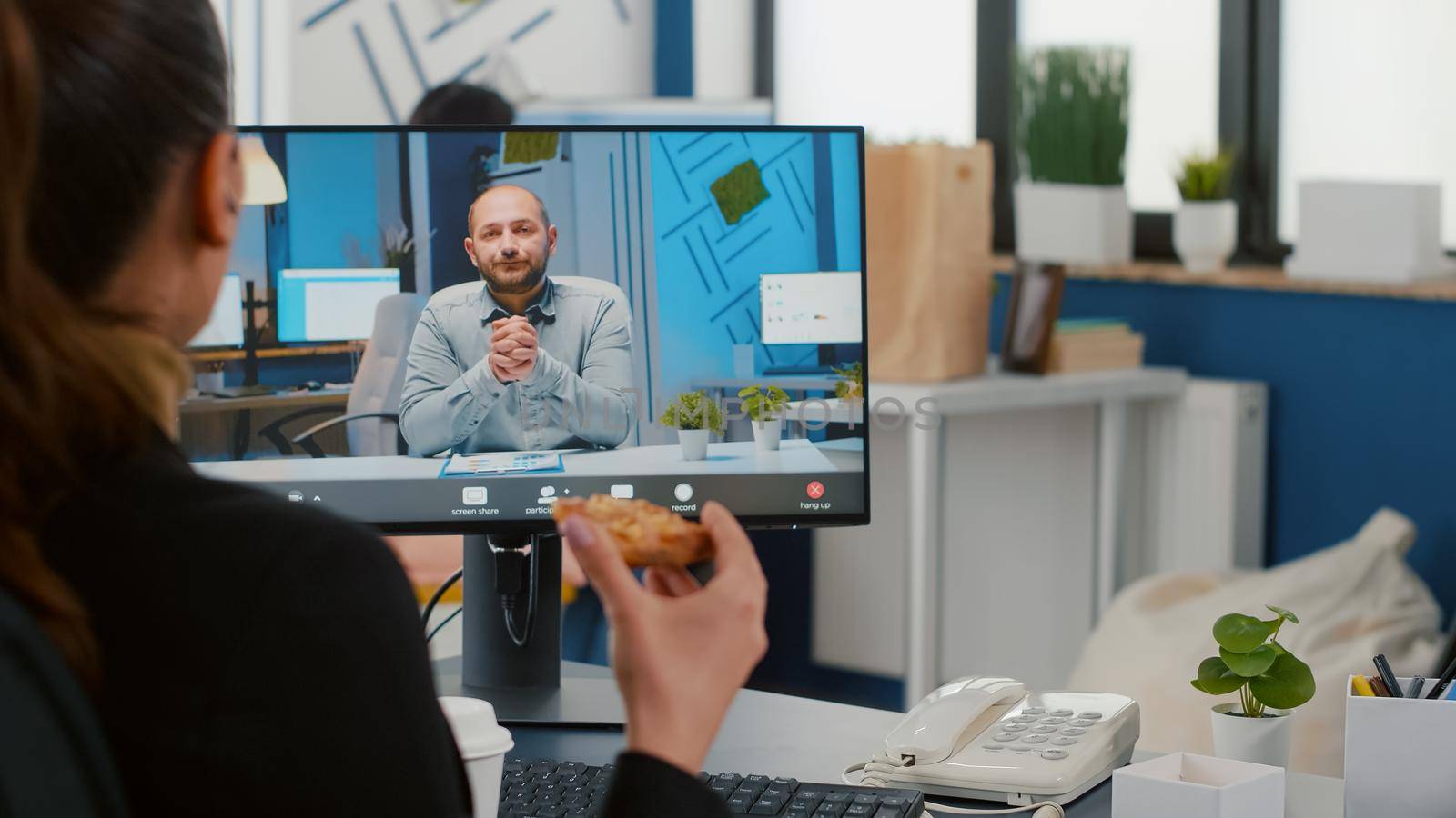 Businesswoman discussing with remote entrepreneur during online videocall meeting conference having delivery lunch meal break. Entrepreneur eating pizza and drinking coffee at desk in company office