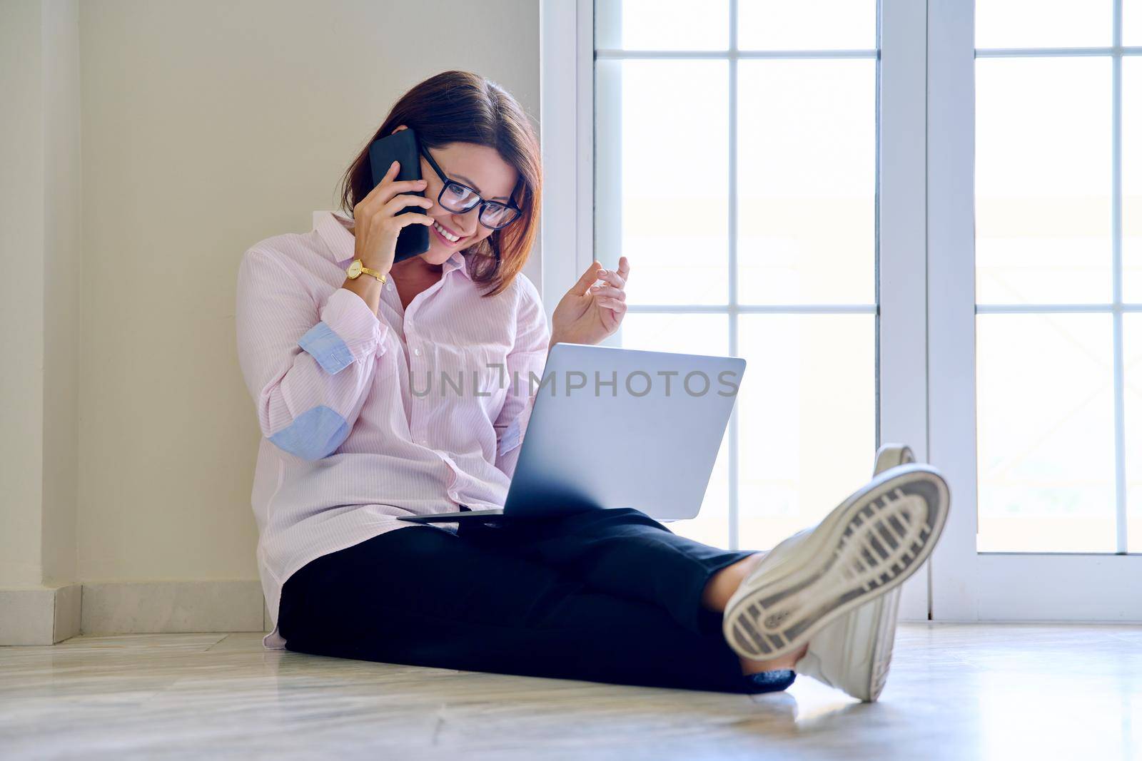 Business woman sitting on floor with laptop talking on smartphone, home office. Female psychologist counselor teacher mentor therapist analyst working online. Technology in business education medicine