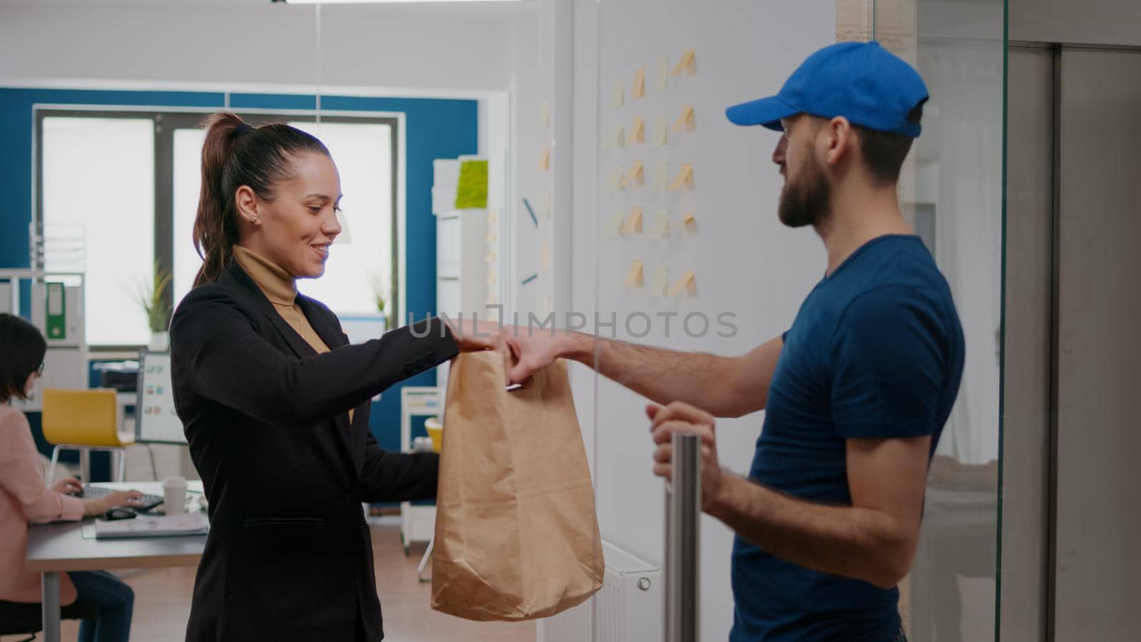 Delivery man giving takeaway package with food order to businesswoman working in startup business company office. Takeout fastfood delivery in corporate job place, lunch meal break paper bag