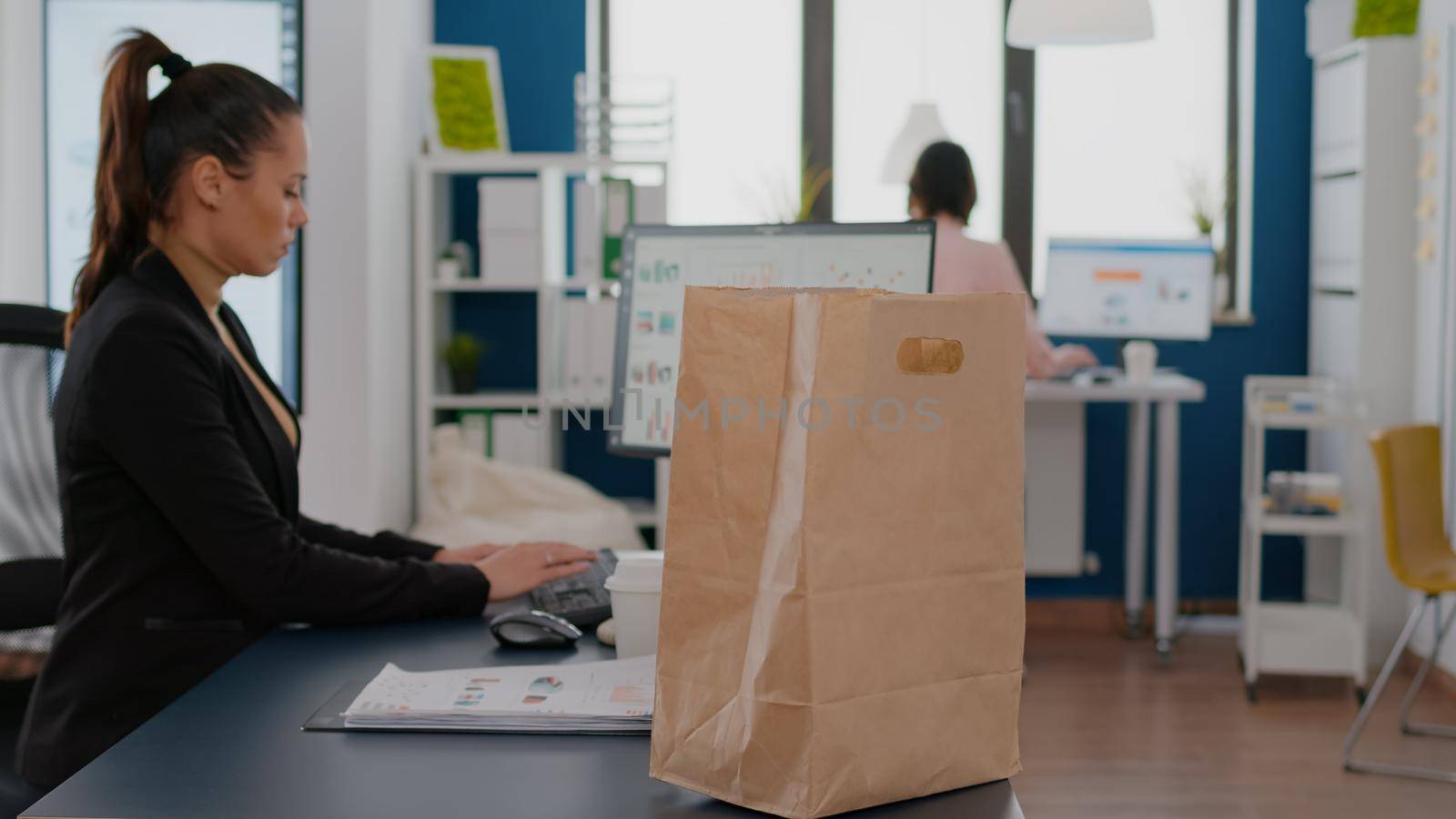 Businesswoman holding paper bag with takeaway food meal order putting on desk during takeout lunchtime in company office. Delivery man delivering fastfood packet for businesspeople