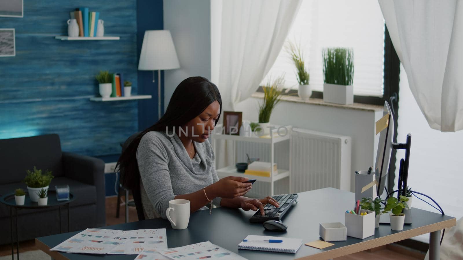 Black woman holding electronic credit card typing online payment on computer by DCStudio