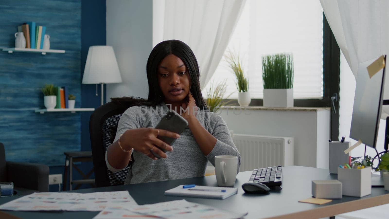 Cheerful black student smiling while taking selfie with smartphone sitting at desk table in living room posing on social media. Attractive young woman relaxing browsing blogger photo on internet