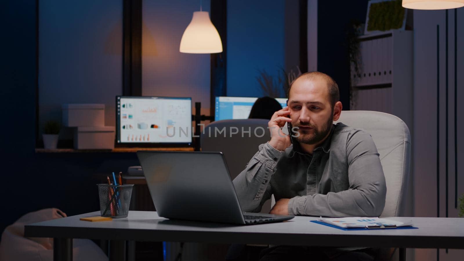 Exhausted businessman sitting at desk table discussing management ideas gesturing during negotiations phone call working late at night in company office. Entrepreneur man planning business interview