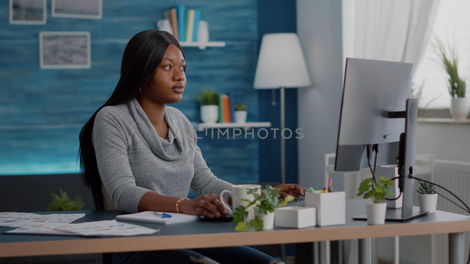 Student with black skin searching online courses writing school homework on on computer during online webinar education. Woman sitting at desk table in living room working remote from home