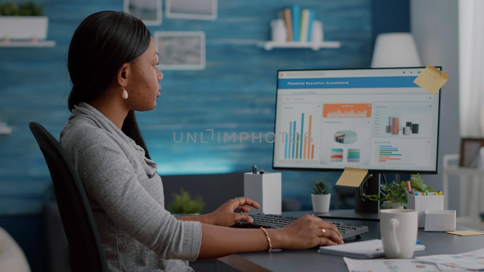 African american student typing financial investment analyzing digital statistics using university online app webinar. Black woman sitting at desk working remote from home at commerce chart on computer