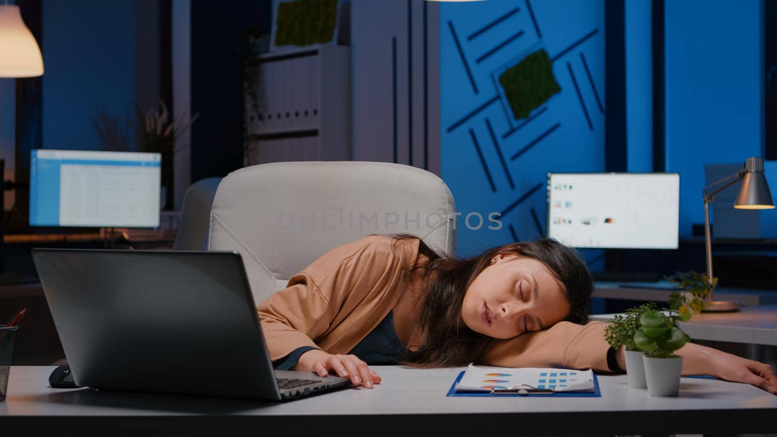 Businesswoman sleeping on desk while working at accounting statistics in business company office late at night. Overworked, stressed exhausted employee at workplace napping on overtime