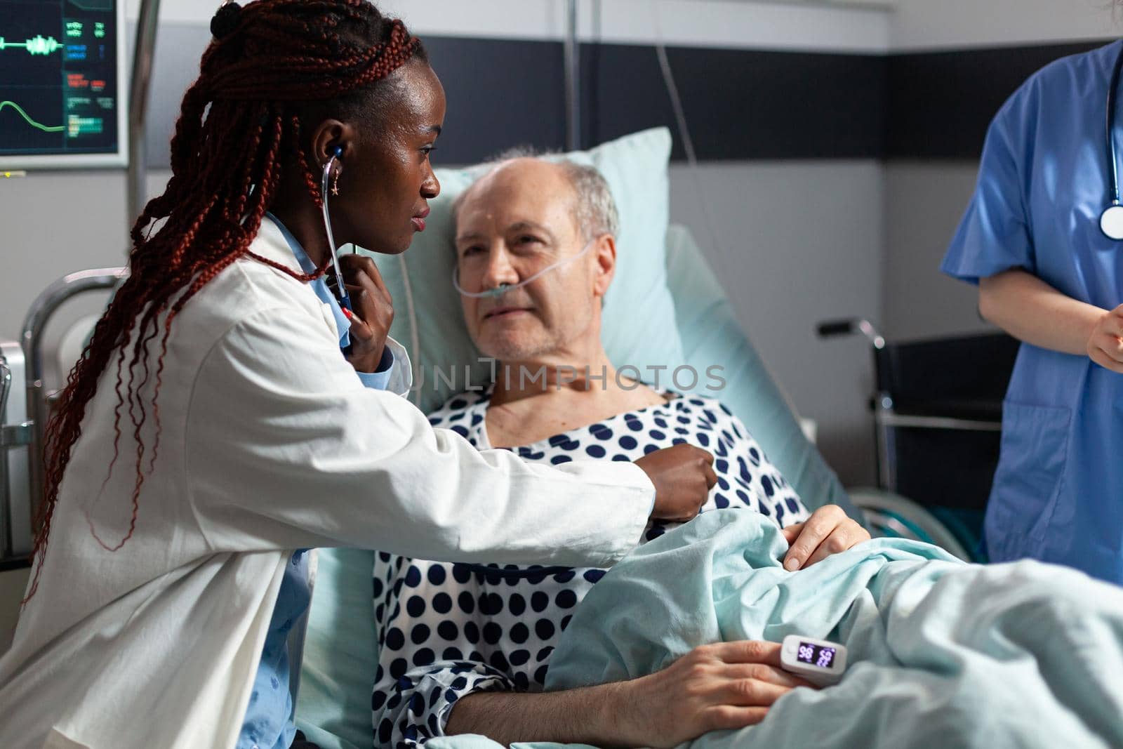 African american cardiologist checking examining senior patient heart, using stethoscope while patient is laying in hospital bed to set diagnosis for therapy, Breathing with help from test tube.