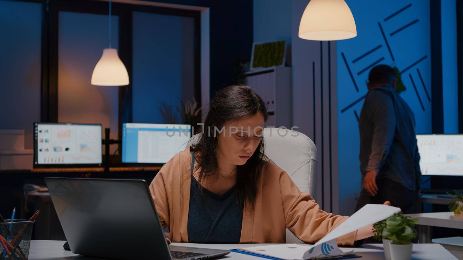 Overworked businesswoman analyzing financial graphs on clipboard by DCStudio