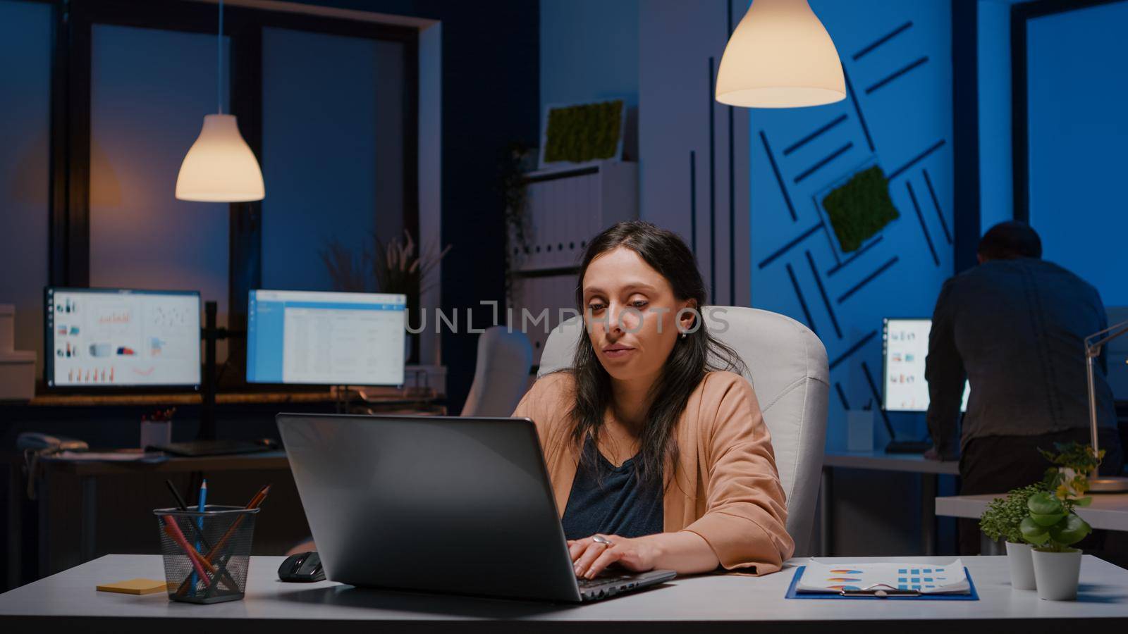 Exhausted workaholic businesswoman yawning while working late at night on laptop before company deadline in startup business office. Stressed overworked frustrated executive manager woman