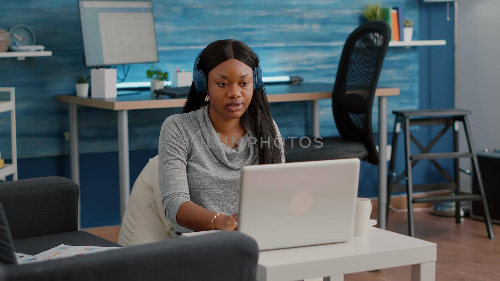 Student blogger with dark skin putting headphones working from home at social media articole by DCStudio