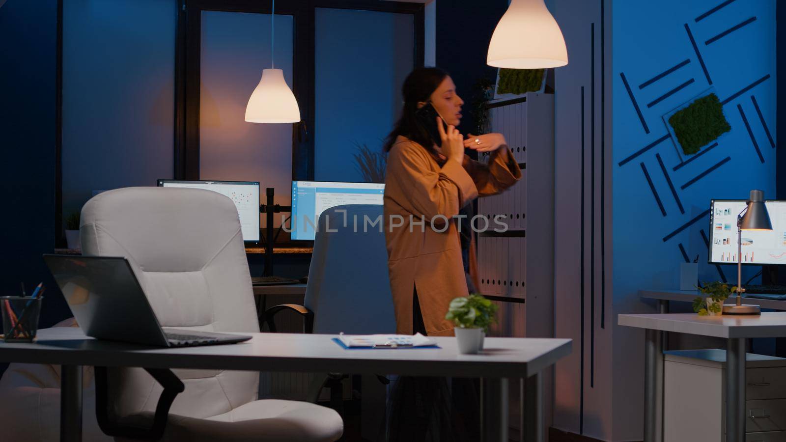 Exhausted businesswoman gesturing while talking at phone discussing marketing strategy late at night in startup office. Manager negotiating management statistics analysing company consultation ideas