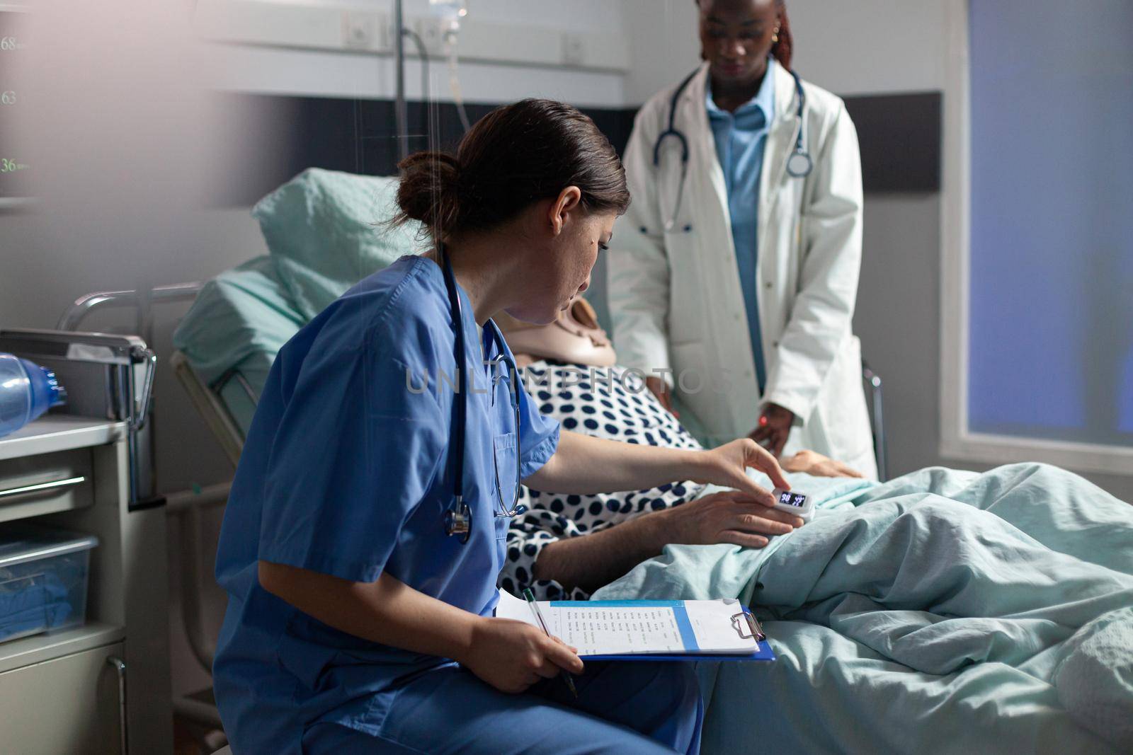 Medical assistant checking oximeter attached to senior man by DCStudio