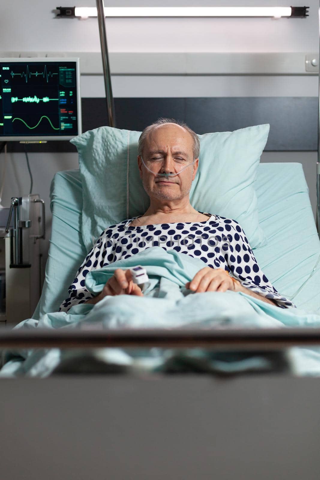 Portrait of sick senior man patient resting in hospital bed, breathing with help from oxygen mask because of lungs infection, having oximeter attached on finger.